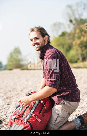 Smiling Young man with backpack sur la rive de galets Banque D'Images