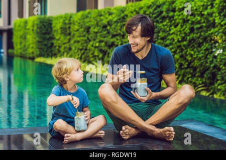 Père et fils manger le dessert avec chia seeds et de mangues à la piscine le matin. la saine alimentation, l'alimentation, les régimes végétariens et personnes concept Banque D'Images
