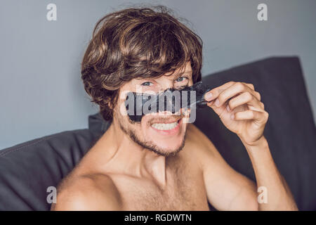 Homme heureux avec masque noir sur le visage. Homme Photo recevant des soins spa. Concept Beauté Soins De La Peau Banque D'Images