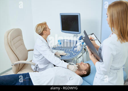 Young man laying on bed durant l'observation médicale sur concultation en clinique privée. Bien spesialist Médecin Professionnel de traiter le patient avec de l'équipement médical avec l'aide de l'infirmière. Banque D'Images