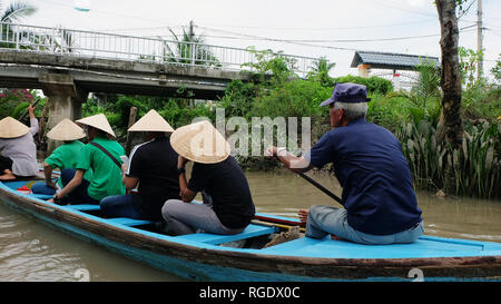 Un vieil homme l'aviron un bateau en bois bleu de l'arrière, avec les passagers portant des chapeaux en bambou assis en face. Banque D'Images