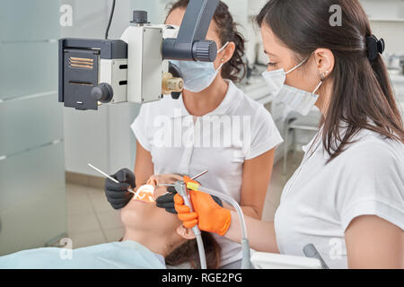 Female patient lying on fauteuil dentaire dentiste dents professionnel alors que le traitement. Médecin expérimenté travaillant avec des équipements modernes et l'assistant d'aider. Concept de stomatologie et de soins. Banque D'Images