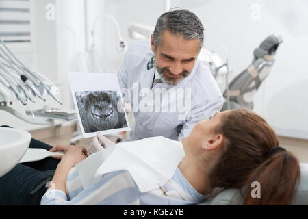Stomatologie médecin montrant la radiographie dentaire du patient à la mâchoire, consulting. Young woman lying on dentiste, président à la recherche à l'analyse. Concept de soins des dents et de stomatologie. Banque D'Images