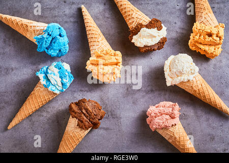 Spécialité délicieux cornets de crème glacée avec une variété de saveurs différentes disposés comme une nature morte sur un fond gris ardoise Banque D'Images