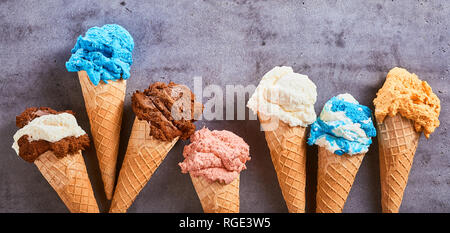 Bannière d'été avec une ligne d'un assortiment de spécialités aromatisées ice cream cones sur un fond gris ardoise texturé Banque D'Images