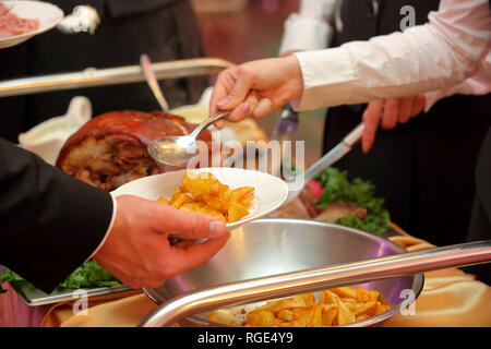 Serveur sert de viande rôtie et pommes de terre au four à la fête ou réception de mariage Banque D'Images