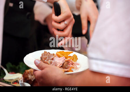 Serveur sert de viande rôtie et pommes de terre au four à la fête ou réception de mariage Banque D'Images