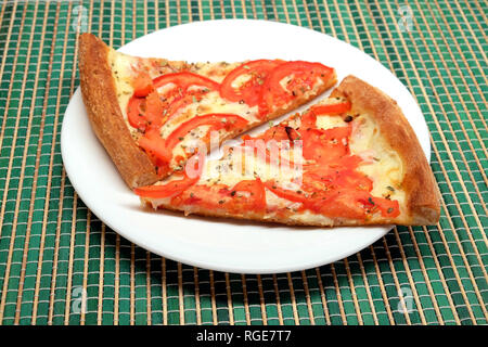 Deux morceaux de pizza appétissante sur plaque blanche sur le tapis en rotin vert closeup Banque D'Images