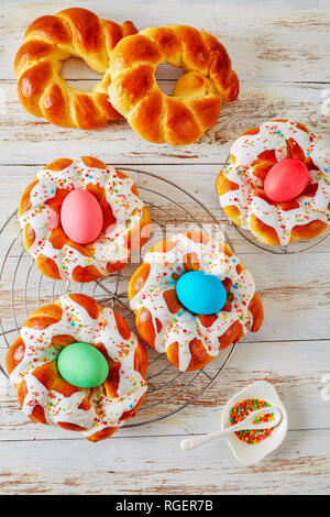 Pain de Pâques italienne vitrée anneaux autour d'oeufs teints et surmontée de sprinkles colorés sur une grille, sur une vieille table en bois blanc, vue verticale de Banque D'Images