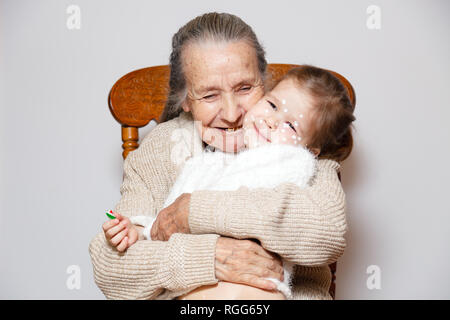 Сute grand-mère aux cheveux gris avec des dents en or en chandail tricoté câlins petite-fille avec la varicelle, les points blancs, des cloques sur le visage. Concept family phot Banque D'Images