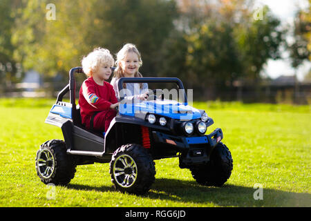 Petite voiture électrique de conduite pour les enfants en été. Jouets de plein air. Les enfants dans l'alimentation de la batterie du véhicule. Little Boy and girl riding camion jouet dans le jardin. Fam Banque D'Images