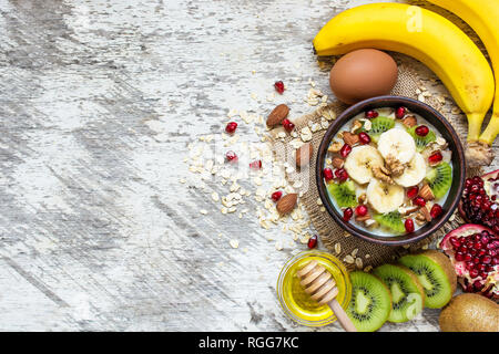 Gruau d'avoine avec bananes, kiwis, grenades, les noix et le miel dans un bol avec l'oeuf pour petit-déjeuner sain on white background. Vue de dessus Banque D'Images