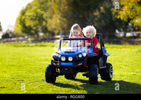 Petite voiture électrique de conduite pour les enfants en été. Jouets de plein air. Les enfants dans l'alimentation de la batterie du véhicule. Little Boy and girl riding camion jouet dans le jardin. Fam Banque D'Images