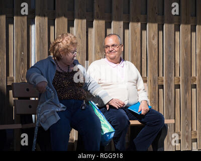 Un couple assis sur un banc. L'homme sourit agréablement à la femme comme elle atteint pour sa part. Tourné à la Texas State Aquarium. Banque D'Images