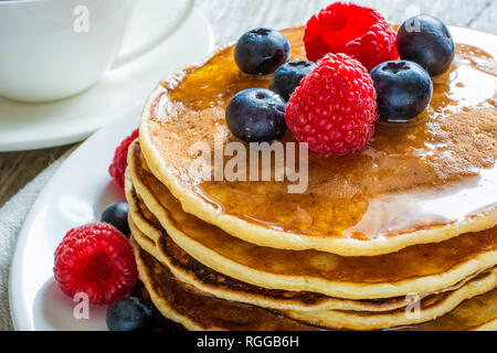 Pile de crêpes avec les baies fraîches et de miel sur fond de bois rustique avec une tasse à café pour le petit déjeuner Banque D'Images