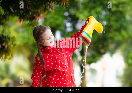 Avec des bottes en caoutchouc pour enfants jouant dans la pluie en automne parc. Enfant en flaque boueuse par temps pluvieux jour d'automne. Botte de ville pleine d'eau. Petite fille en veste rouge Banque D'Images