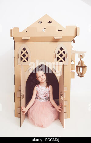 Petite Princesse en couronne joue avec son château en carton. Une émotion vraie du bonheur de l'enfant. Banque D'Images