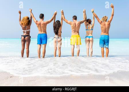 Groupe d'amis à la plage, debout dans la mer avec les bras levés Banque D'Images