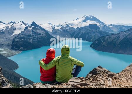 Vue du Panorama Ridge trail, deux randonneurs assis sur un rocher avec Garibaldi Lake, lac glaciaire, turquoise et la montagne de la Garde Banque D'Images