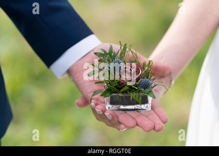 Boîte de verre décorée de fleurs avec les anneaux de mariage dans les mains de la jeunes mariés, Close up Banque D'Images