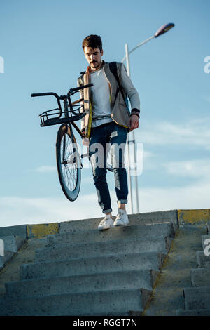 Jeune homme de banlieue transport vélo fixie descendant des escaliers Banque D'Images