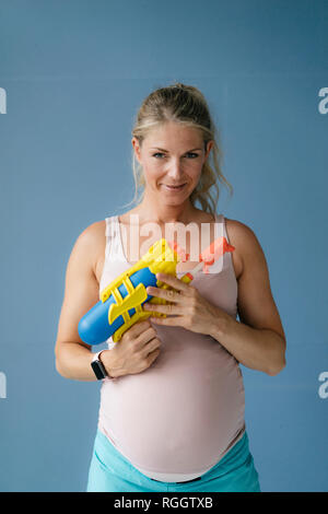 Portrait of smiling pregnant woman holding water gun Banque D'Images