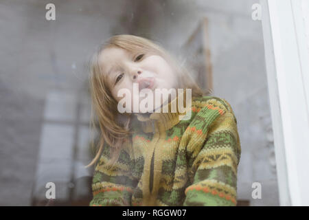 Portrait of little girl sticking out tongue tout en regardant par la fenêtre de Banque D'Images