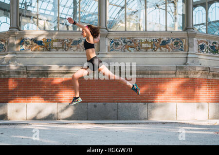 Full body of young fit female in black sports bra and shorts performing  stretching exercise for neck and doing head side bend while working out on  paved square Stock Photo - Alamy