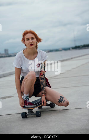 Portrait of young woman crouching sur carver skateboard sur une promenade Banque D'Images