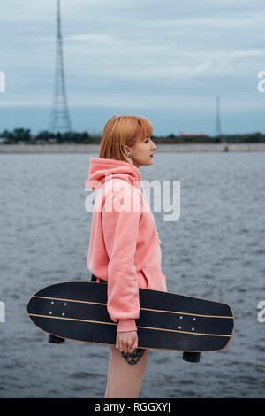 Young woman holding carver skateboard debout à la Riverside Banque D'Images