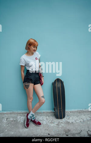 Cool Jeune femme debout à côté de mur turquoise carver skateboard Banque D'Images