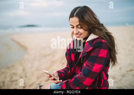 Smiling young woman using smartphone sur la plage Banque D'Images