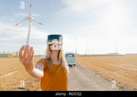 Jeune femme avec des lunettes en VR camping-van in rural landscape holding modèle d'éolienne Banque D'Images