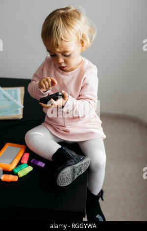 Petite fille à l'aide de téléphone mobile, sitting on desk Banque D'Images