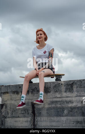 Jeune femme assise sur un mur de béton sur carver skateboard Banque D'Images