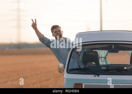 Jeune homme excité de faire signe de la main la victoire le camping-car dans la fenêtre paysage rural Banque D'Images