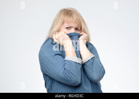 Blonde girl in pull bleu tirant son chandail à la mode sur la tête. Banque D'Images