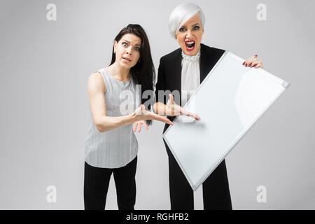 Portrait de deux femmes féroce avec tableau magnétique blanc vide dans les mains isolé sur fond blanc. Un lieu d'une étiquette Banque D'Images