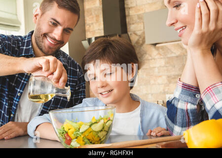 Mère Père et fils à la maison debout s'appuyant sur le tableau dans la cuisine ensemble garçon close-up à la papa à l'ajout d'huile pour salade close-up smiling curieux. Banque D'Images