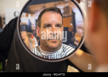 Un mec est heureux de vérifier sa nouvelle coupe fraîche dans un miroir à la coiffure Banque D'Images