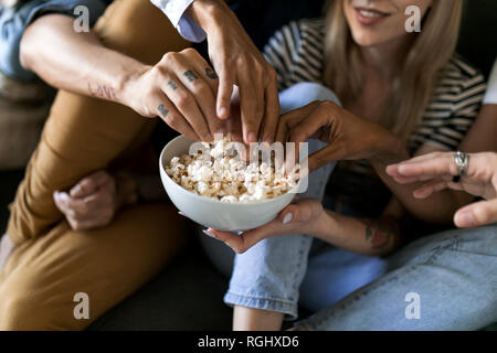 Close-up of friends sitting on couch le partage d'un bol de maïs soufflé Banque D'Images