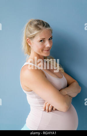 Portrait of pregnant woman standing at mur bleu Banque D'Images