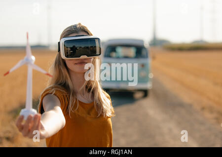 Jeune femme avec des lunettes en VR camping-van in rural landscape holding modèle d'éolienne Banque D'Images