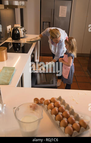 Vue de côté de mère avec sa fille pour supprimer les cookies du four dans la cuisine à la maison Banque D'Images