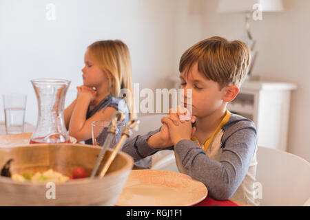 Frères et sœurs priant avant d'avoir de la nourriture sur table à manger Banque D'Images