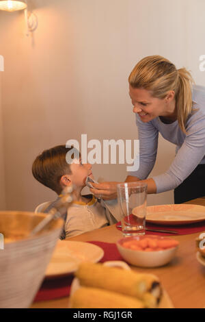 Vue latérale d'essuyage mère fils la bouche avec une serviette sur une table à manger à la maison Banque D'Images