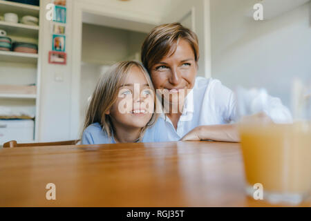 Smiling mother and daughter sitting at table de cuisine à la maison Banque D'Images