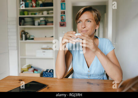 Femme assise à table à la maison avec une tasse de café Banque D'Images