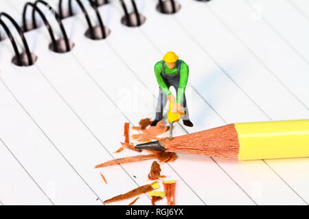 Diorama conceptuel image d'une figure miniature en affinant un crayon sur un carnet de notes Banque D'Images