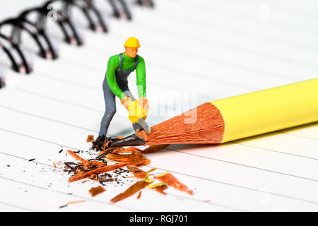 Diorama conceptuel image d'une figure miniature en affinant un crayon sur un carnet de notes Banque D'Images